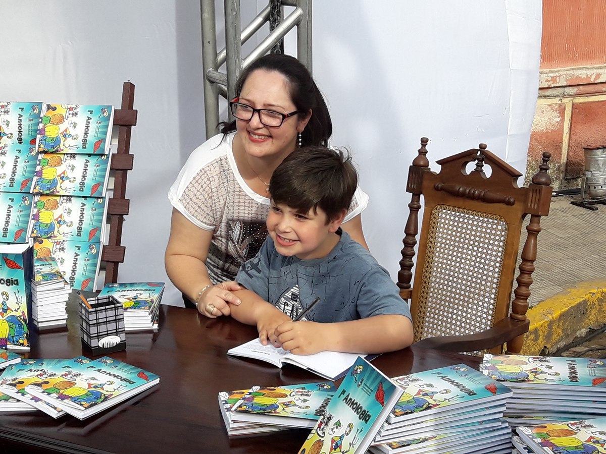 Aluno autografa exemplar da Antologia ao lado de familiar.